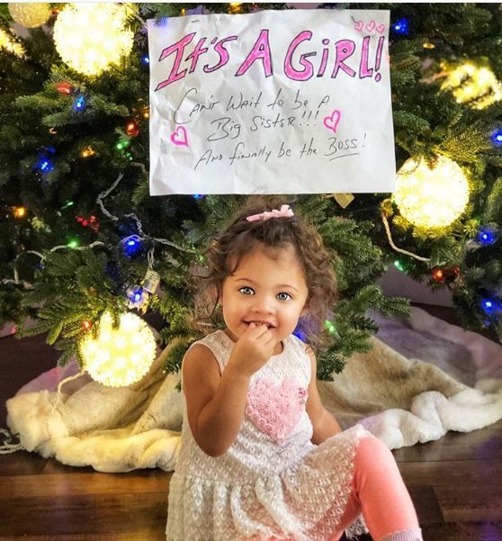 The Rock's daughter Jasmine in front of a sign announcing he's expecting his third child