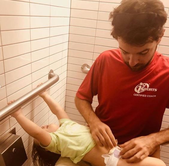 Father squatting to change daughter's diaper.