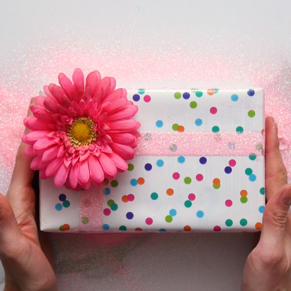 Birthday gift wrapped in multi colored polka dot paper finished with light pink glitter and a bright pink flower