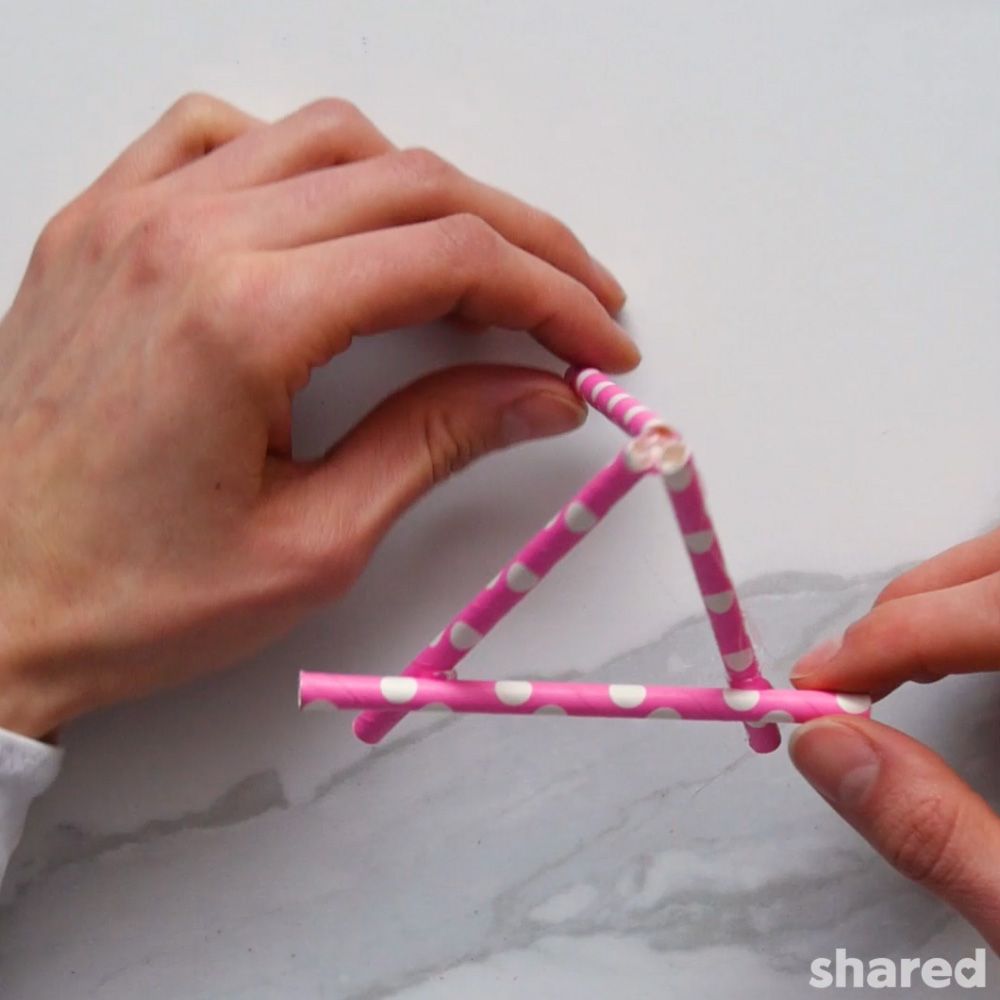 hands creating a mini easel card holder out of pink paper straws