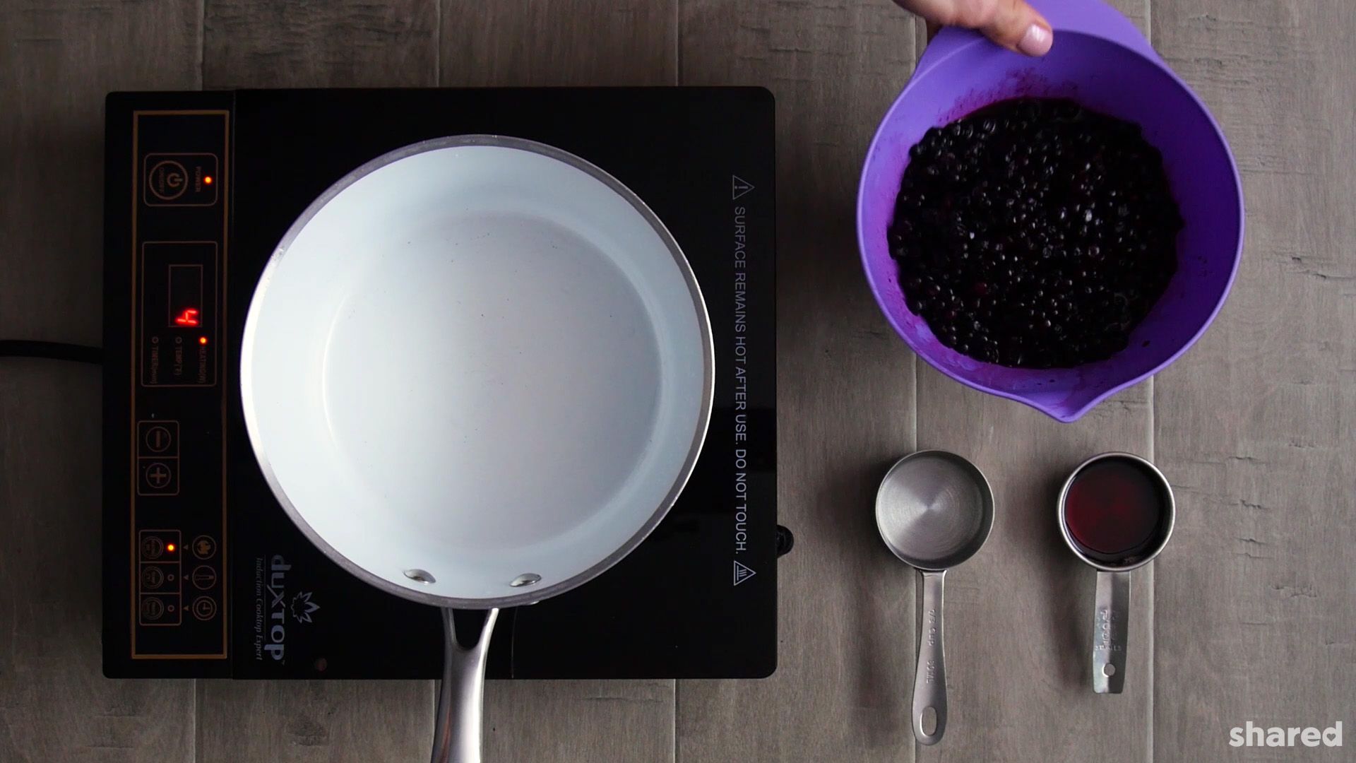 photo may contain a white saucepan on a stove top beside a purple bowl with frozen blueberries and and two stainless measuring cups of water and maple syrup