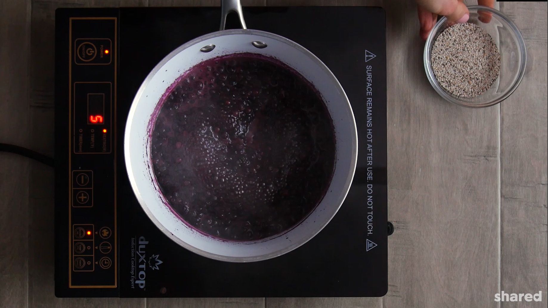 blueberry chia jam in a white saucepan simmering on a stove top