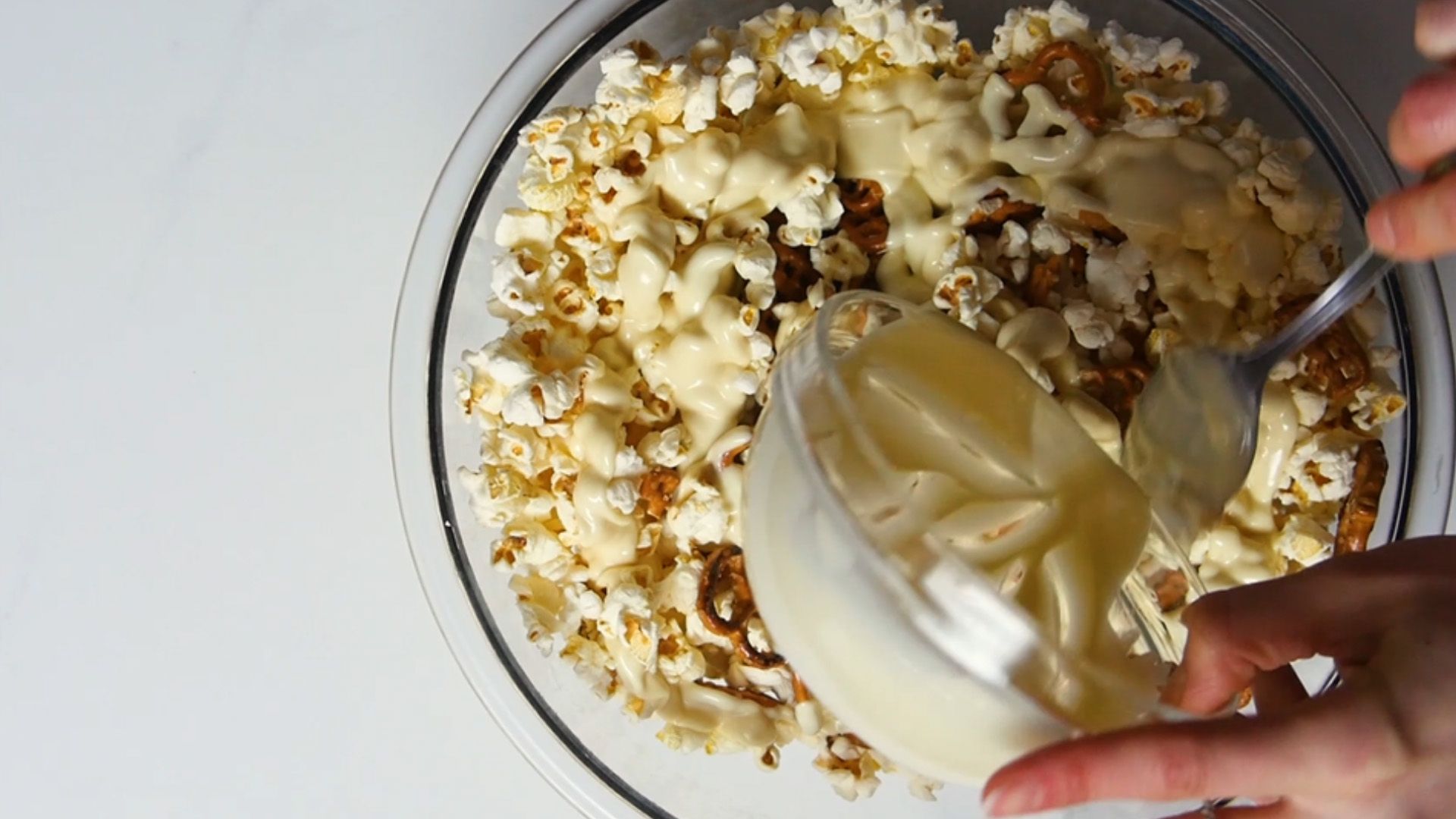 white chocolate being poured onto popcorn and pretzels