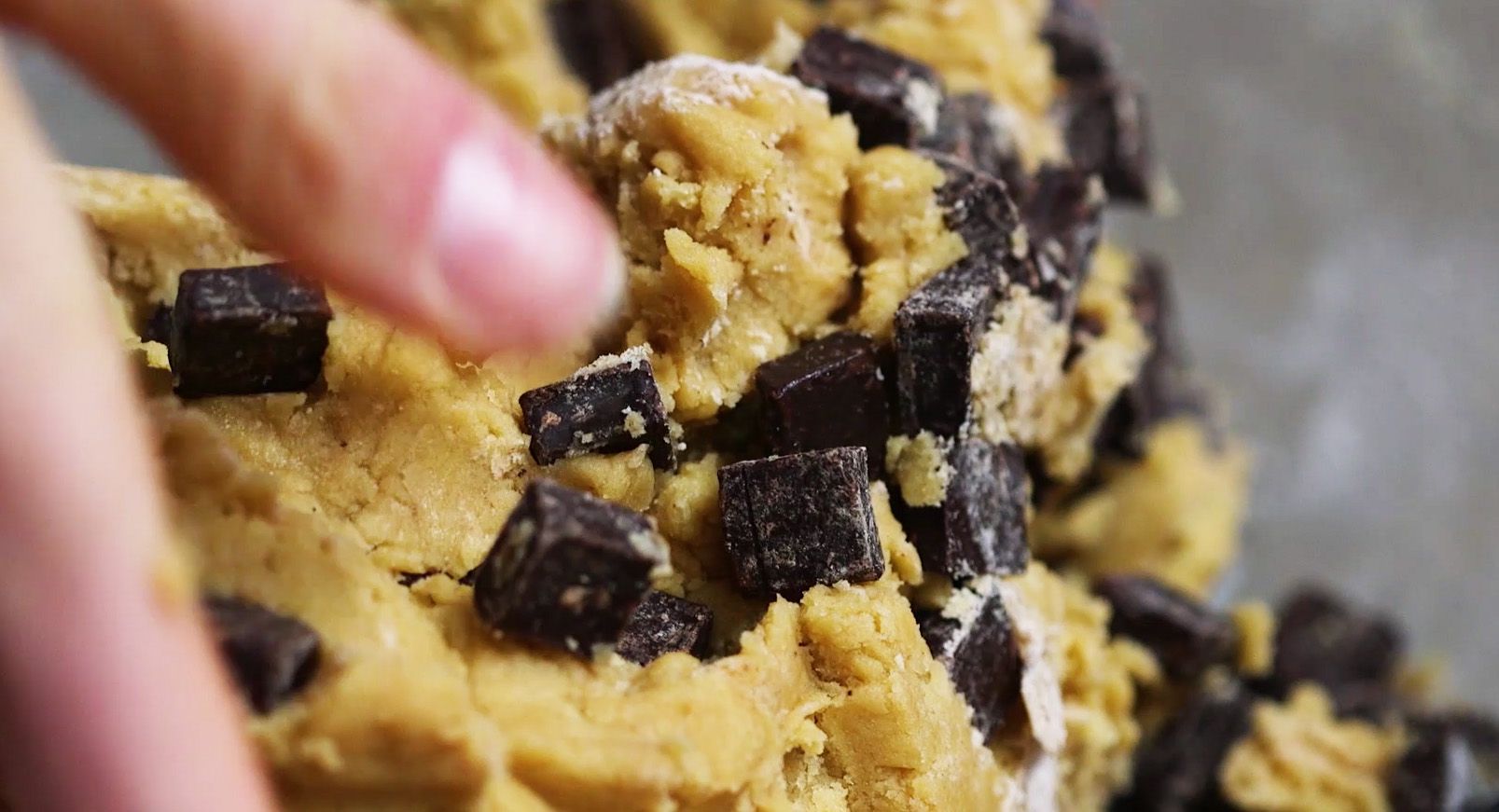 close up of hands mixing chocolate chunks into cookie batter