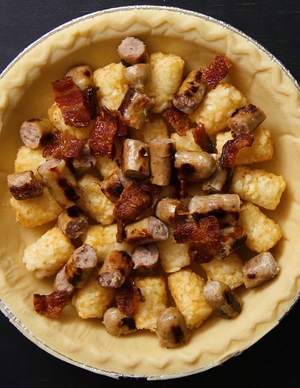uncooked pie crust filled with tater tots, breakfast sausage and cut bacon