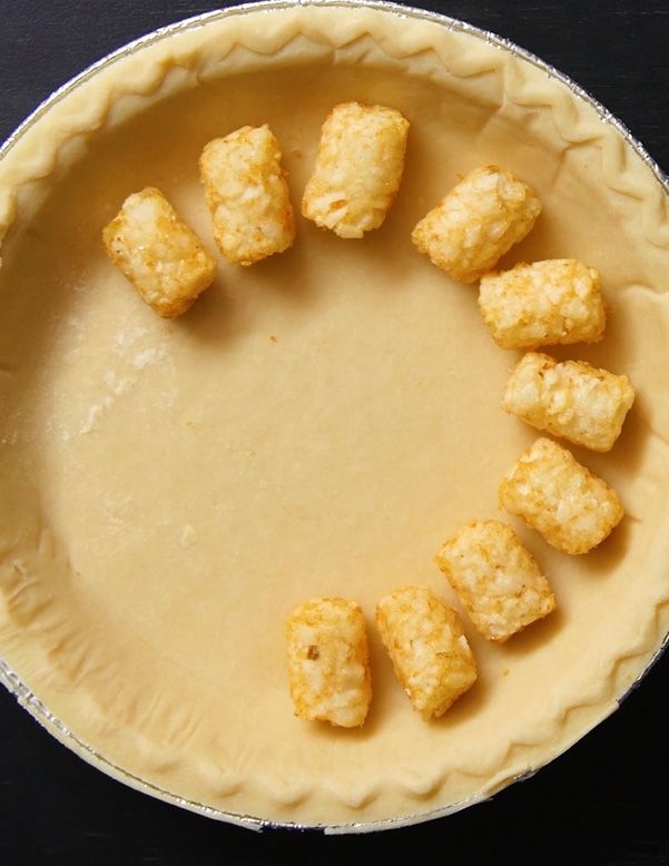 unbaked pie crust being lined with tater tots