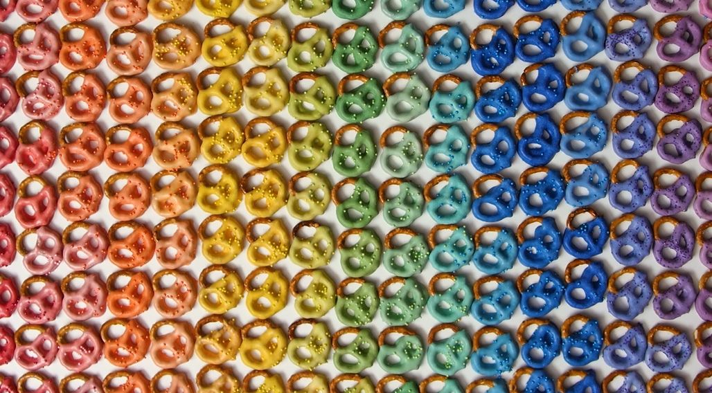 hundreds of chocolate covered pretzels in the colors of the rainbow lined up next to each other