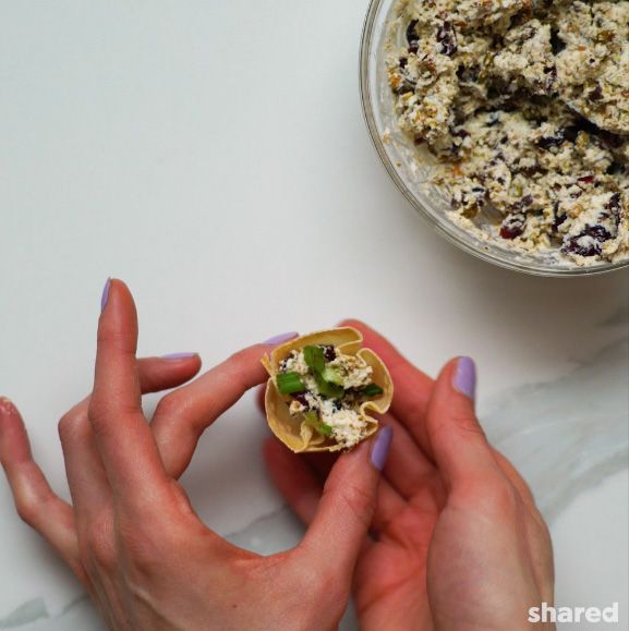 filled wonton cup topped with green herbs being held in a hand