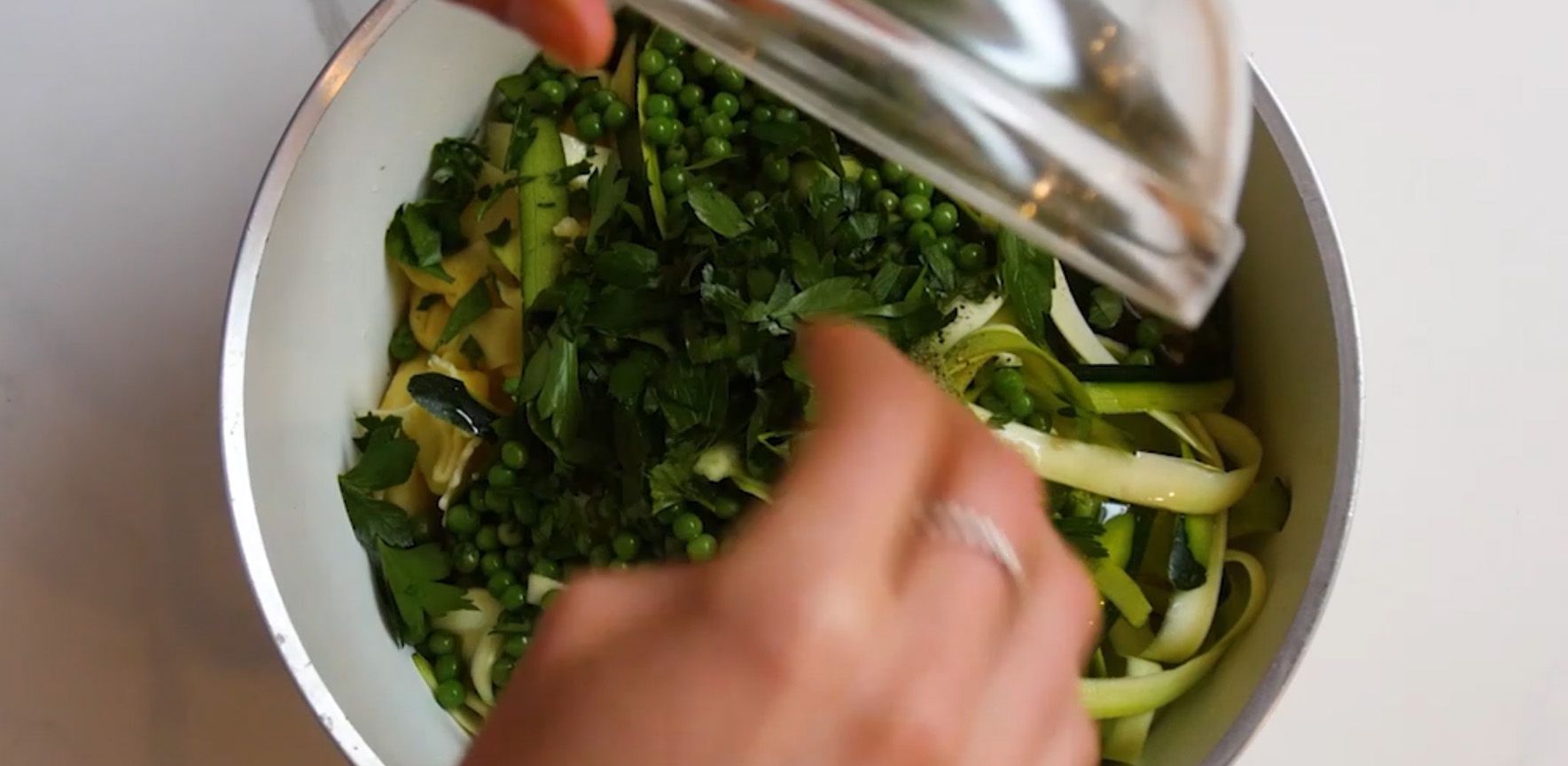 Green herbs and peas being added to pasta salad