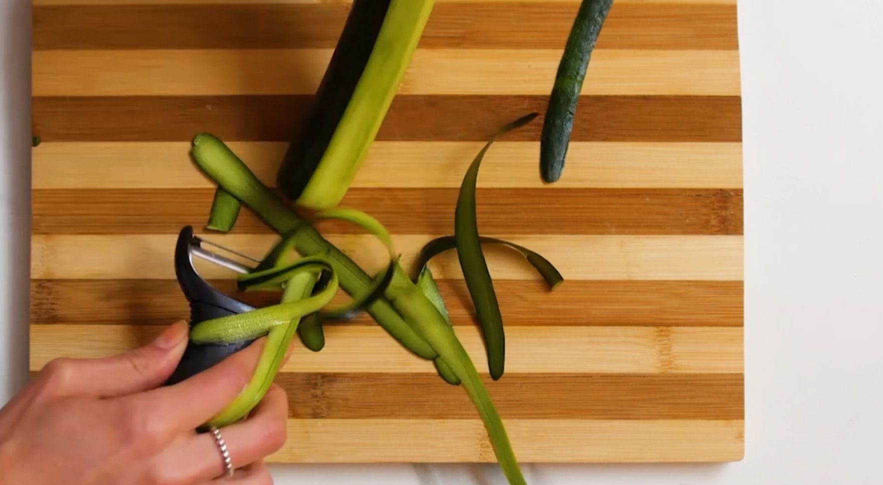 small green zucchini being peeled into strips over a cutting board 