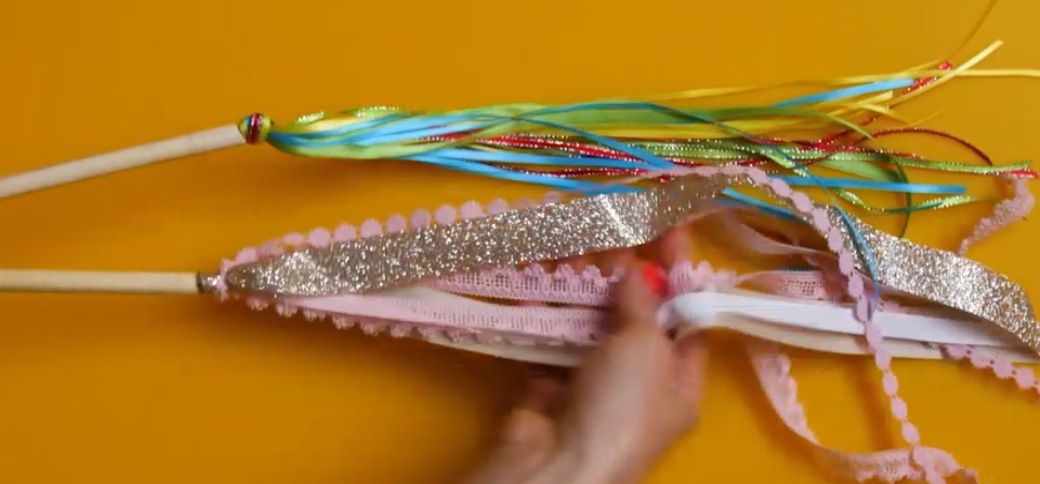 a pink and rainbow colored ribbon wand on a yellow background