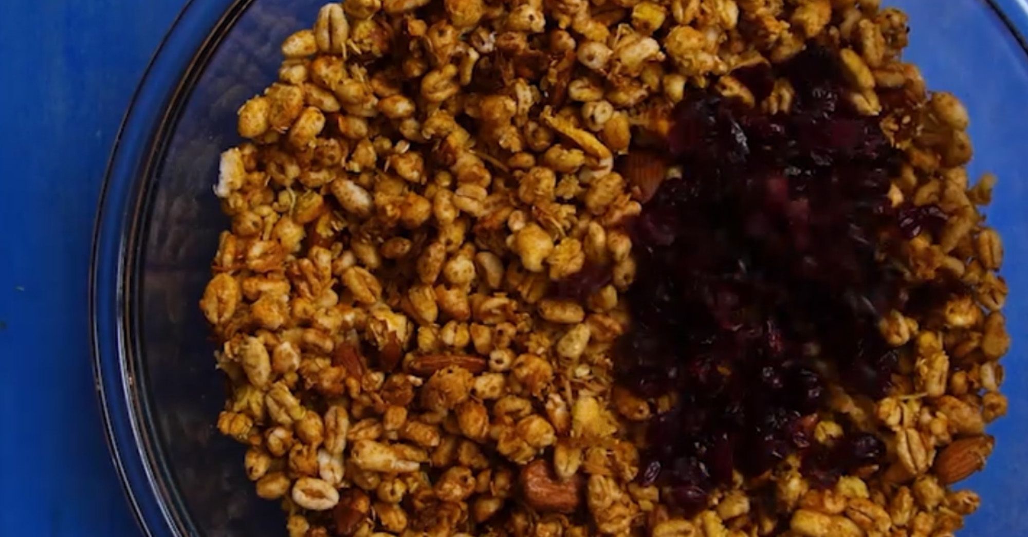 dried cranberries being added to cooked granola in a glass bowl