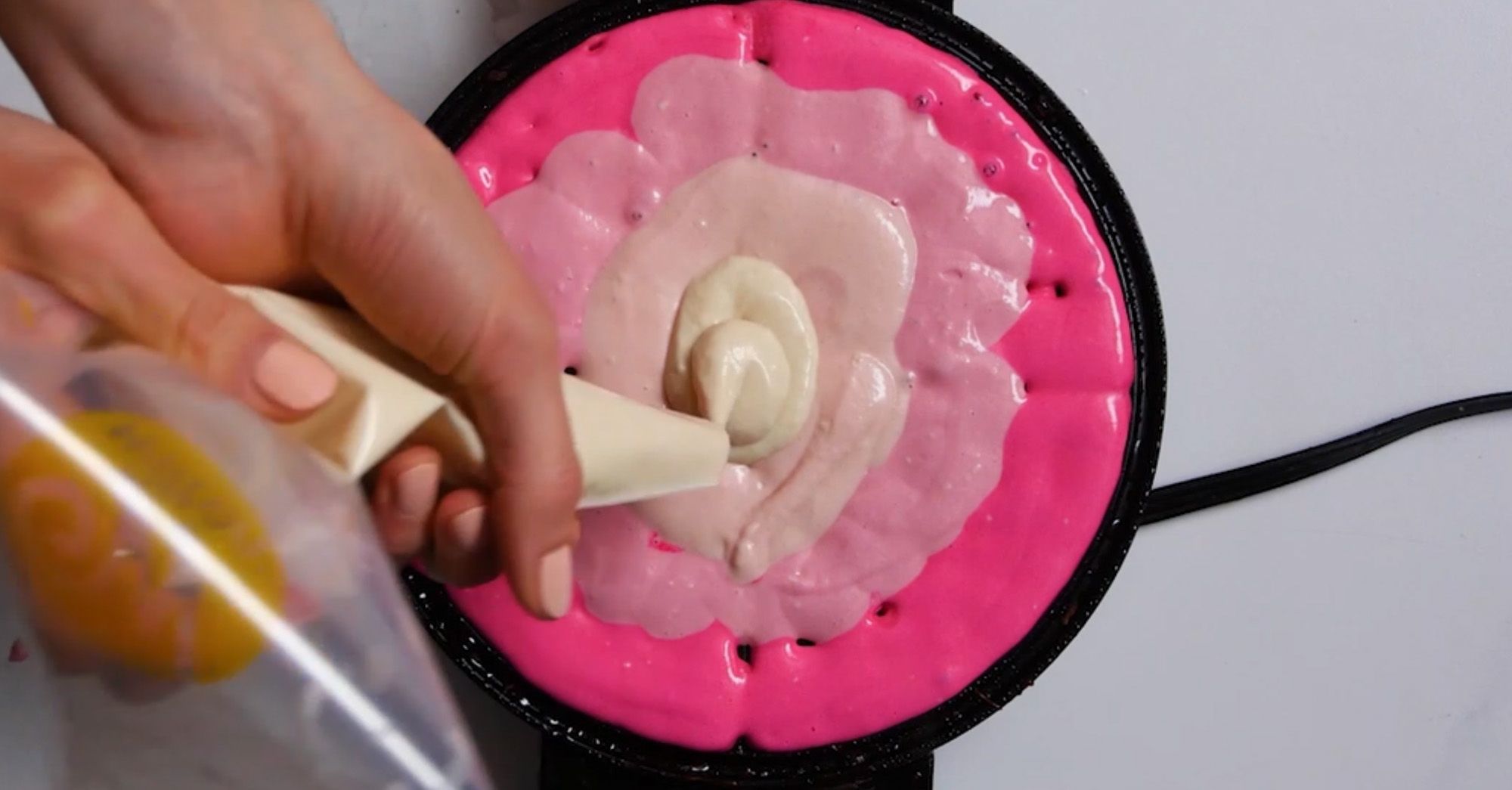 pink ombre waffle batter being squeezed from a piping bag into a waffle iron