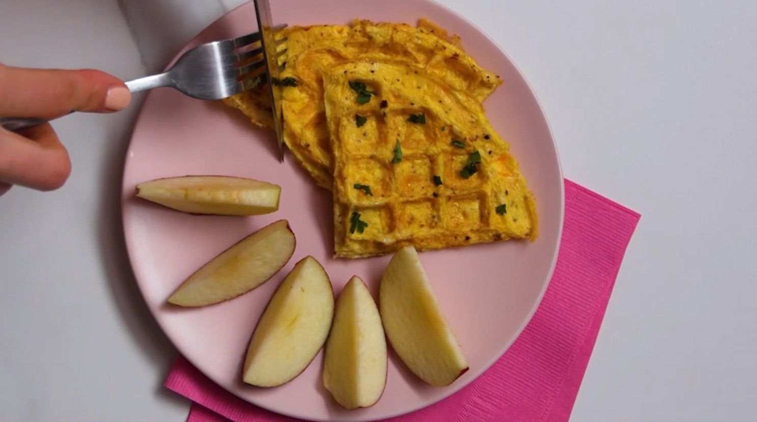 waffle omelette and red apple slices on a pink plate with dark pink napkins